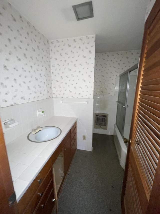 bathroom with bath / shower combo with glass door, tile walls, heating unit, and vanity