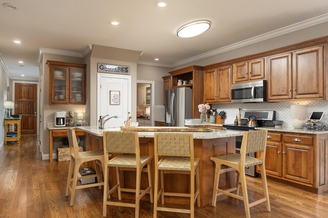 kitchen with appliances with stainless steel finishes, light stone counters, light hardwood / wood-style floors, a breakfast bar area, and a center island with sink