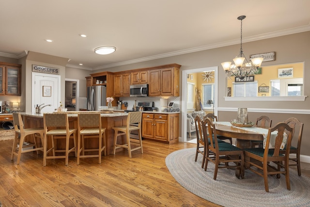 kitchen featuring light wood-type flooring, a notable chandelier, ornamental molding, decorative light fixtures, and stainless steel appliances