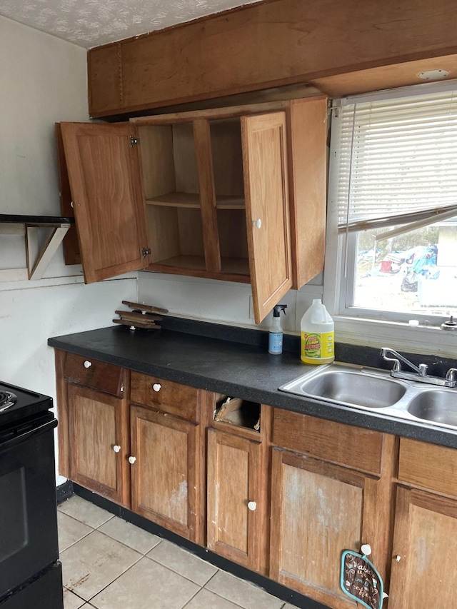 kitchen featuring dark countertops, brown cabinets, black range with electric stovetop, and a sink