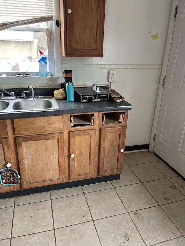 kitchen with dark countertops, brown cabinets, a sink, and light tile patterned flooring