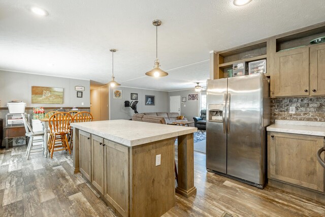 kitchen with stainless steel refrigerator with ice dispenser, hardwood / wood-style floors, a kitchen island, and ceiling fan