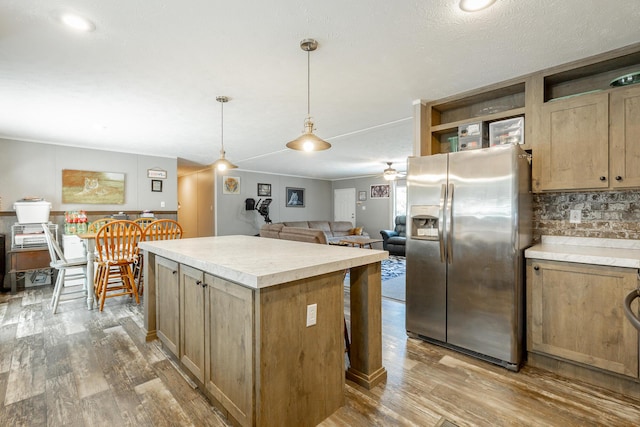 kitchen with light countertops, wood finished floors, open shelves, stainless steel fridge with ice dispenser, and a center island