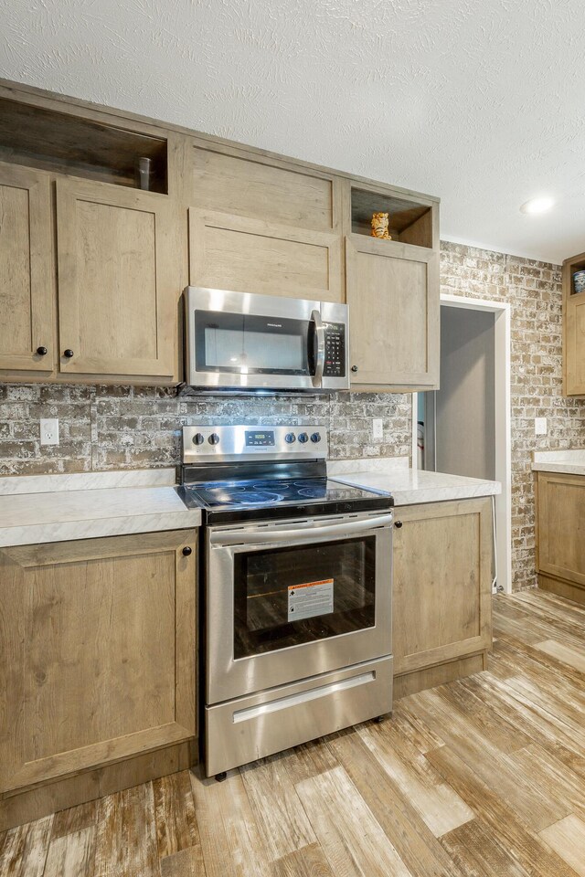 kitchen with a textured ceiling, brick wall, appliances with stainless steel finishes, and light hardwood / wood-style floors