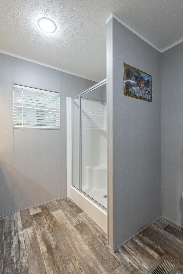 bathroom with a shower stall, a textured ceiling, crown molding, and wood finished floors