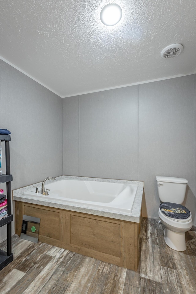 bathroom with wood finished floors, toilet, a textured ceiling, visible vents, and a bath