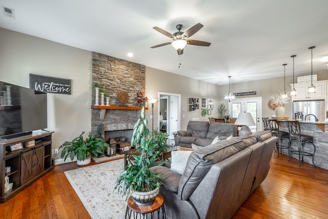 living room featuring ceiling fan with notable chandelier, a fireplace, and wood-type flooring