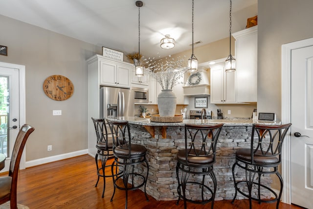 kitchen featuring dark wood-type flooring, appliances with stainless steel finishes, hanging light fixtures, and light stone countertops