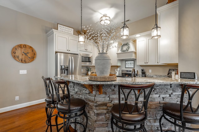 kitchen featuring decorative light fixtures, light stone counters, stainless steel appliances, dark wood-type flooring, and a breakfast bar area