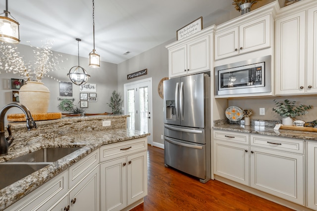 kitchen with hanging light fixtures, light stone counters, stainless steel appliances, dark hardwood / wood-style flooring, and sink