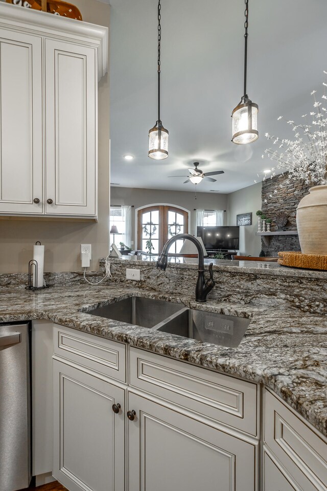 kitchen featuring stainless steel dishwasher, sink, white cabinetry, ceiling fan, and light stone counters