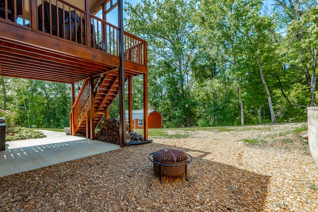 view of yard featuring a deck, a patio area, a storage shed, and an outdoor fire pit