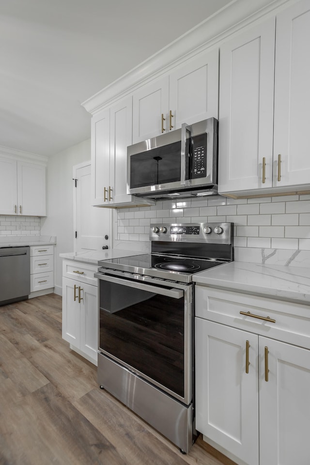 kitchen with light wood-type flooring, appliances with stainless steel finishes, white cabinetry, and decorative backsplash