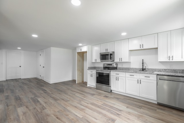 kitchen featuring light wood-type flooring, appliances with stainless steel finishes, light stone countertops, white cabinetry, and sink