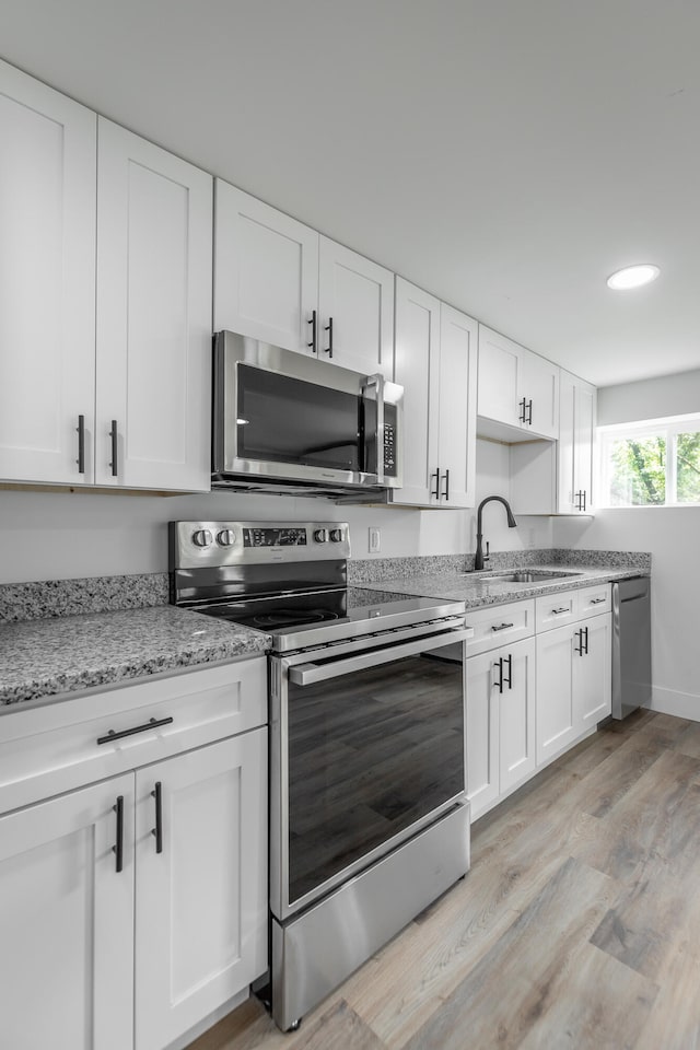 kitchen with light wood-type flooring, white cabinetry, stainless steel appliances, and sink