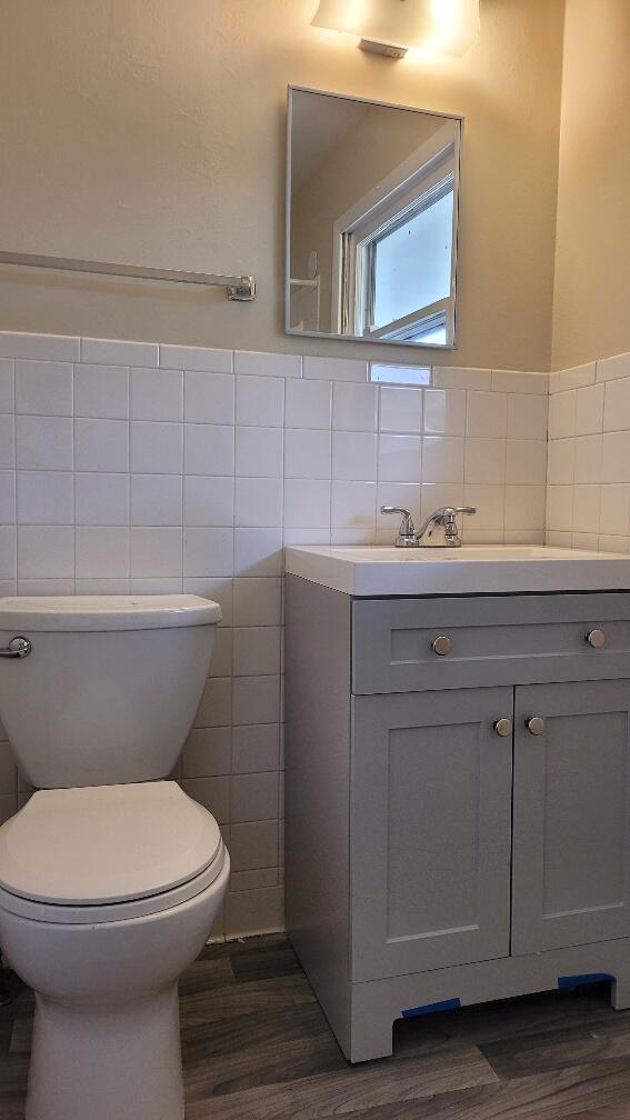 bathroom featuring vanity, toilet, tile walls, and wood-type flooring