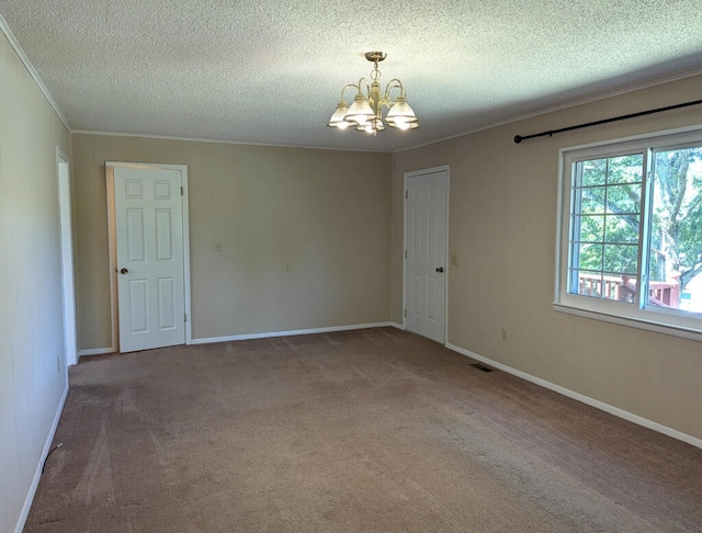 carpeted spare room with a textured ceiling, ornamental molding, and a chandelier