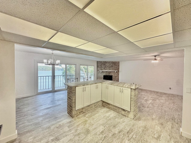 kitchen with a drop ceiling, brick wall, kitchen peninsula, and a brick fireplace