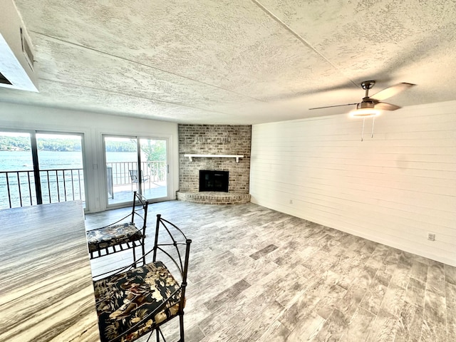 living room featuring hardwood / wood-style flooring, a textured ceiling, a brick fireplace, and ceiling fan