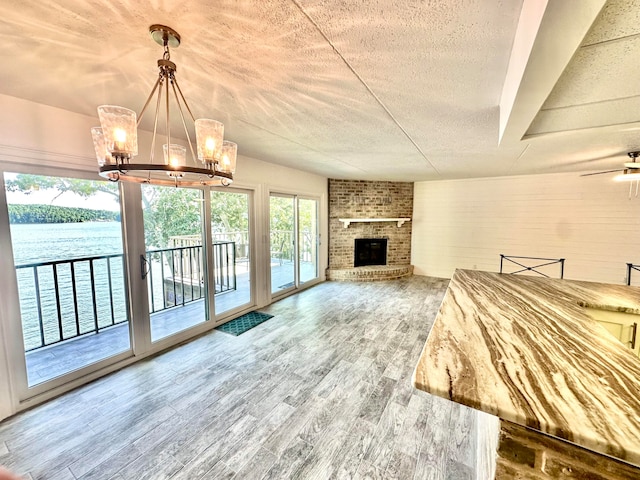 interior space with hardwood / wood-style flooring, a brick fireplace, ceiling fan with notable chandelier, a water view, and a textured ceiling