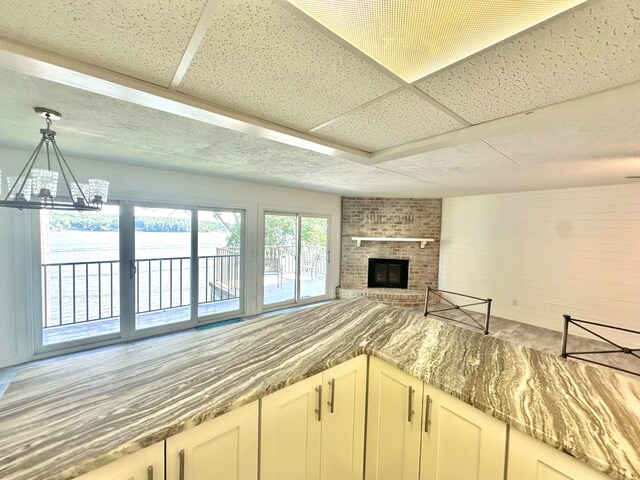 kitchen with a paneled ceiling, brick wall, a notable chandelier, and a brick fireplace