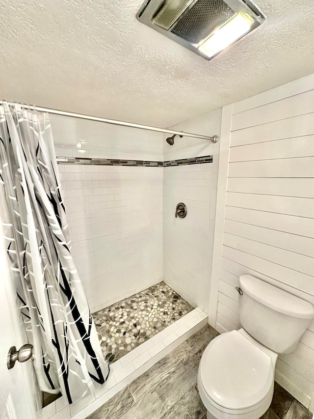 bathroom featuring curtained shower, wooden walls, toilet, wood-type flooring, and a textured ceiling