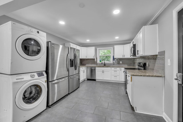 kitchen featuring appliances with stainless steel finishes, stacked washing maching and dryer, tasteful backsplash, sink, and white cabinetry