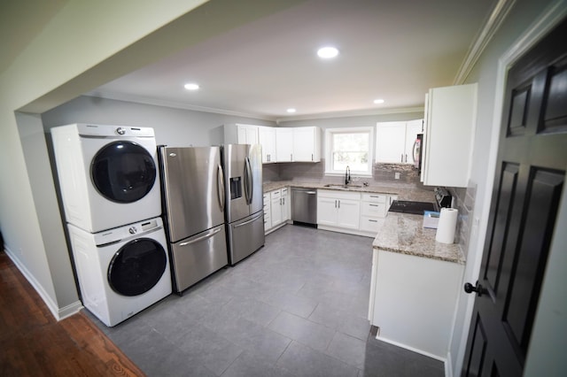 kitchen with backsplash, stainless steel appliances, sink, stacked washer and dryer, and white cabinetry