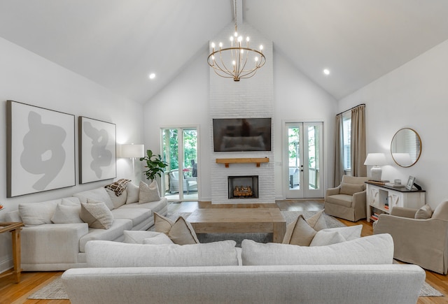 living room featuring high vaulted ceiling, a fireplace, a notable chandelier, and light hardwood / wood-style flooring