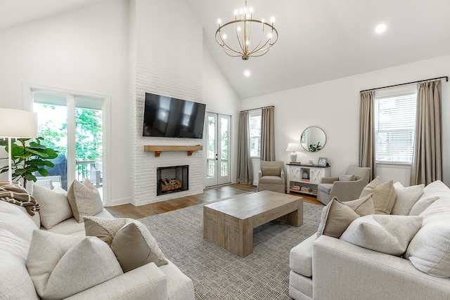 living room with a fireplace, high vaulted ceiling, a chandelier, and light hardwood / wood-style floors