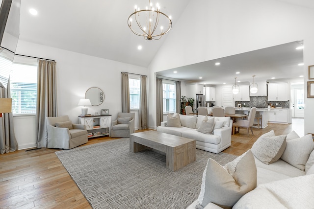 living room with high vaulted ceiling, a chandelier, and light hardwood / wood-style floors