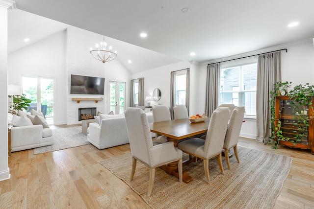 dining room featuring light hardwood / wood-style flooring, an inviting chandelier, high vaulted ceiling, and a fireplace