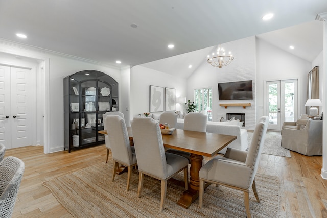 dining space featuring an inviting chandelier, a brick fireplace, light wood-type flooring, french doors, and high vaulted ceiling