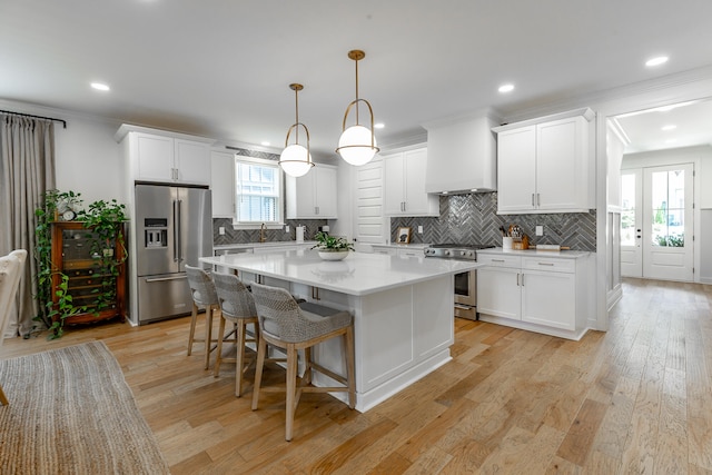 kitchen featuring decorative light fixtures, stainless steel appliances, white cabinets, and light hardwood / wood-style floors