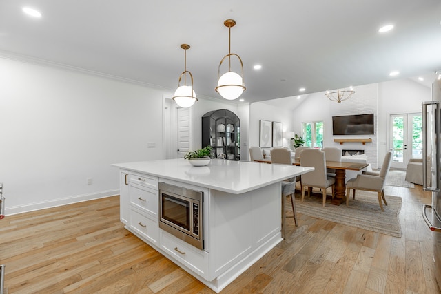 kitchen with white cabinets, a center island, hanging light fixtures, lofted ceiling, and stainless steel microwave