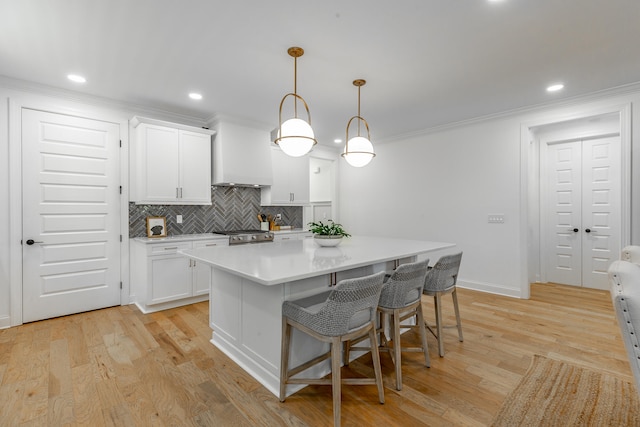 kitchen with hanging light fixtures, light hardwood / wood-style floors, white cabinetry, a kitchen bar, and a kitchen island