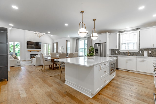 kitchen with appliances with stainless steel finishes, light hardwood / wood-style flooring, a kitchen island, and a large fireplace