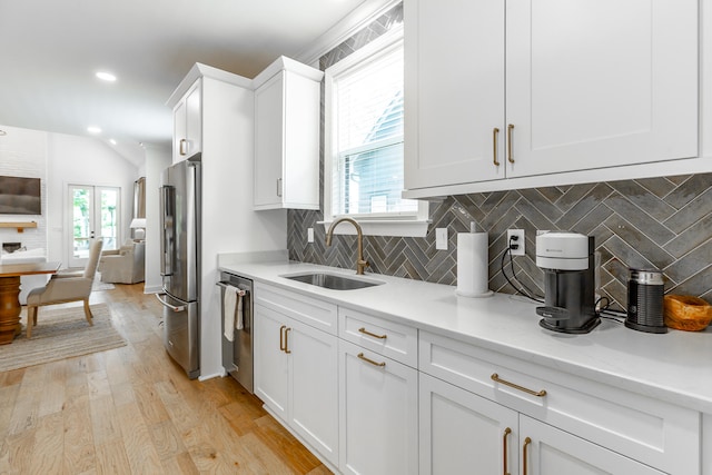 kitchen with white cabinets, backsplash, light hardwood / wood-style flooring, appliances with stainless steel finishes, and sink