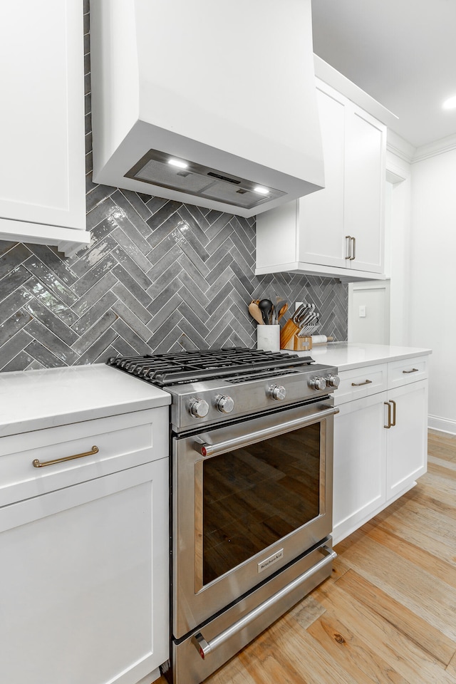 kitchen with white cabinets, light wood-type flooring, high end stove, premium range hood, and decorative backsplash