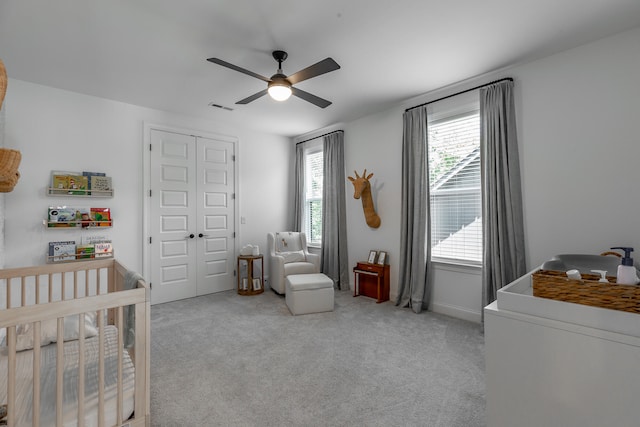 carpeted bedroom featuring ceiling fan and a nursery area