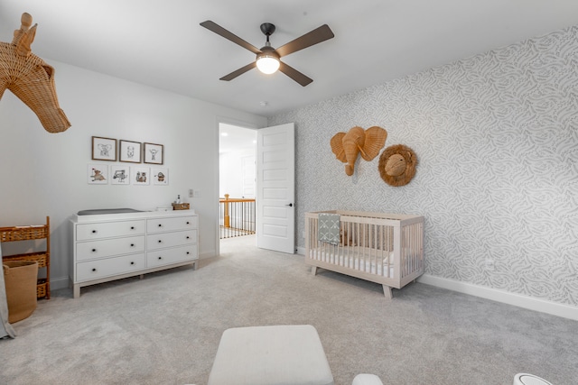 carpeted bedroom with ceiling fan and a nursery area