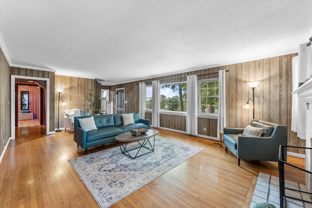 living room with light wood-type flooring, wooden walls, crown molding, and a textured ceiling