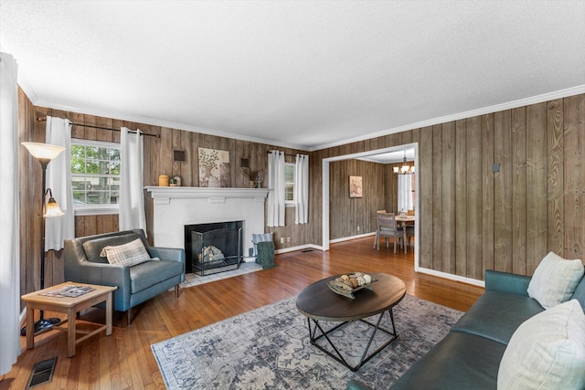 living room with wooden walls, crown molding, a textured ceiling, a chandelier, and hardwood / wood-style flooring