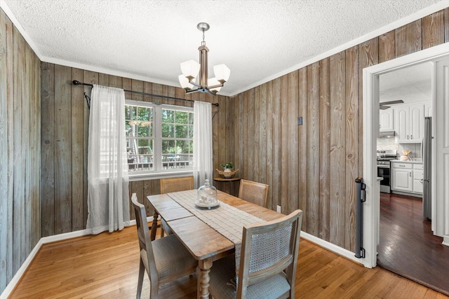 dining room with wood-type flooring, wooden walls, and an inviting chandelier