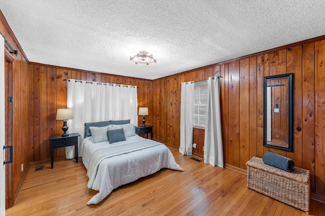 bedroom featuring wooden walls, light hardwood / wood-style floors, and a textured ceiling