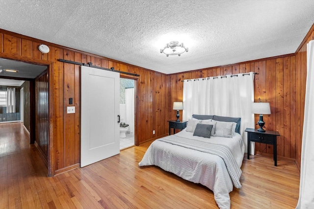 bedroom with a barn door, ensuite bath, light wood-type flooring, and multiple windows