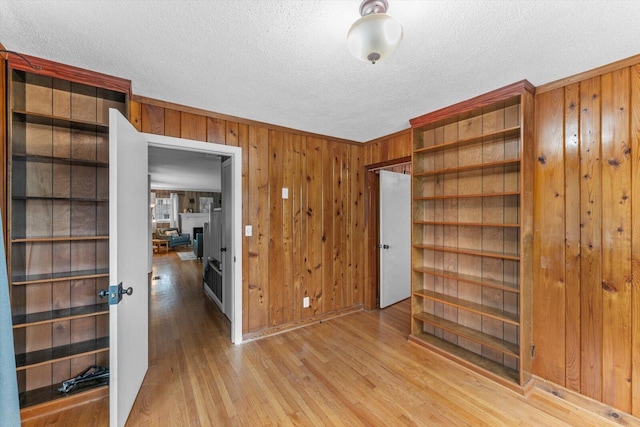 interior space with light wood-type flooring, wood walls, and a textured ceiling