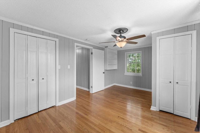 unfurnished bedroom featuring a textured ceiling, ceiling fan, light wood-type flooring, and two closets