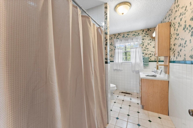 bathroom with a textured ceiling, vanity, curtained shower, tile walls, and toilet