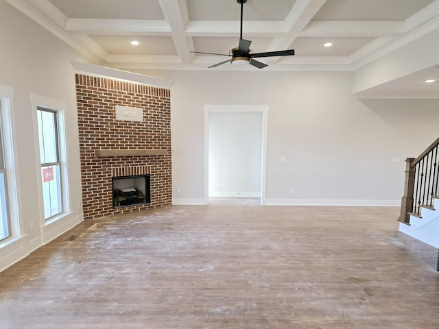 unfurnished living room featuring beamed ceiling, a brick fireplace, coffered ceiling, and light wood-type flooring